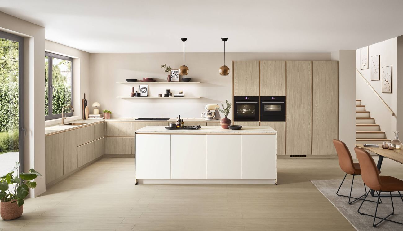 Cocina en roble claro abierta al comedor, con la mesa y las sillas a continuación de la isla